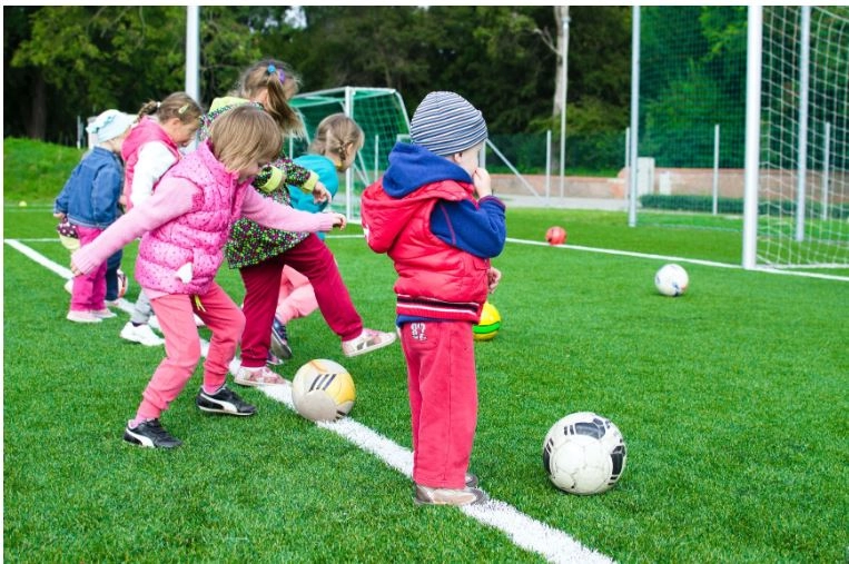 Fotografia d'un grup de xiquets i xiquetes jugant a un camp de futbol